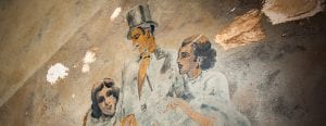 A mural featuring two women locking arms with a man in a top hat.