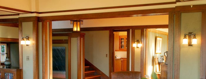 Lit sconces adorn the interior walls of the George Matzen House. The staircase lead up to the next floor is on the left, and some kitchen cabinets can be seen directly ahead.