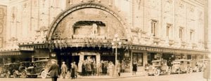 A historic photo of a line of people waiting to enter the Coliseum Theater on the corner of two intersecting streets.
