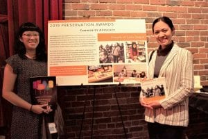 Valerie Tran stands to the left of a board that says "2019 Preservation Awards - Community Advocacy - Friends of Little Saigon." She smiles while she holds a the 2019 Preservation Celebration Benefit journal.